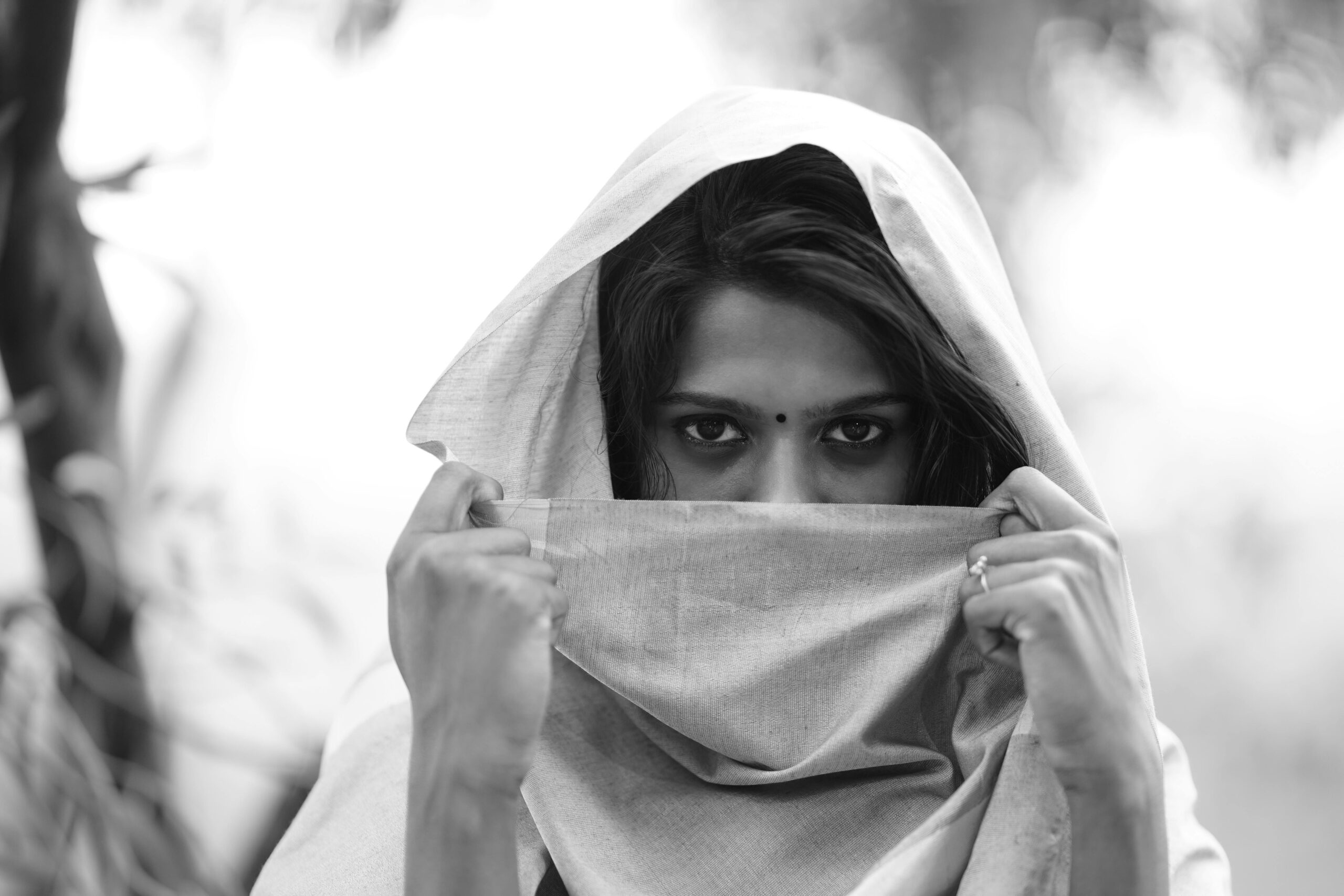 Black and white photo of a woman with a headscarf covering her face, revealing expressive eyes.