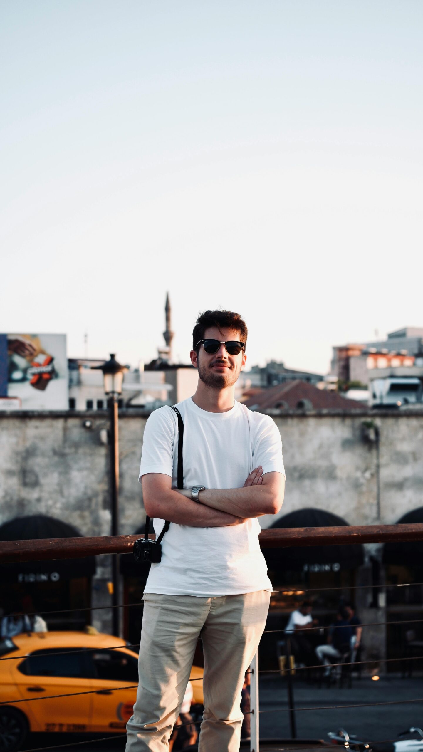 Stylish man in sunglasses and white t-shirt poses in urban street scene during the day.